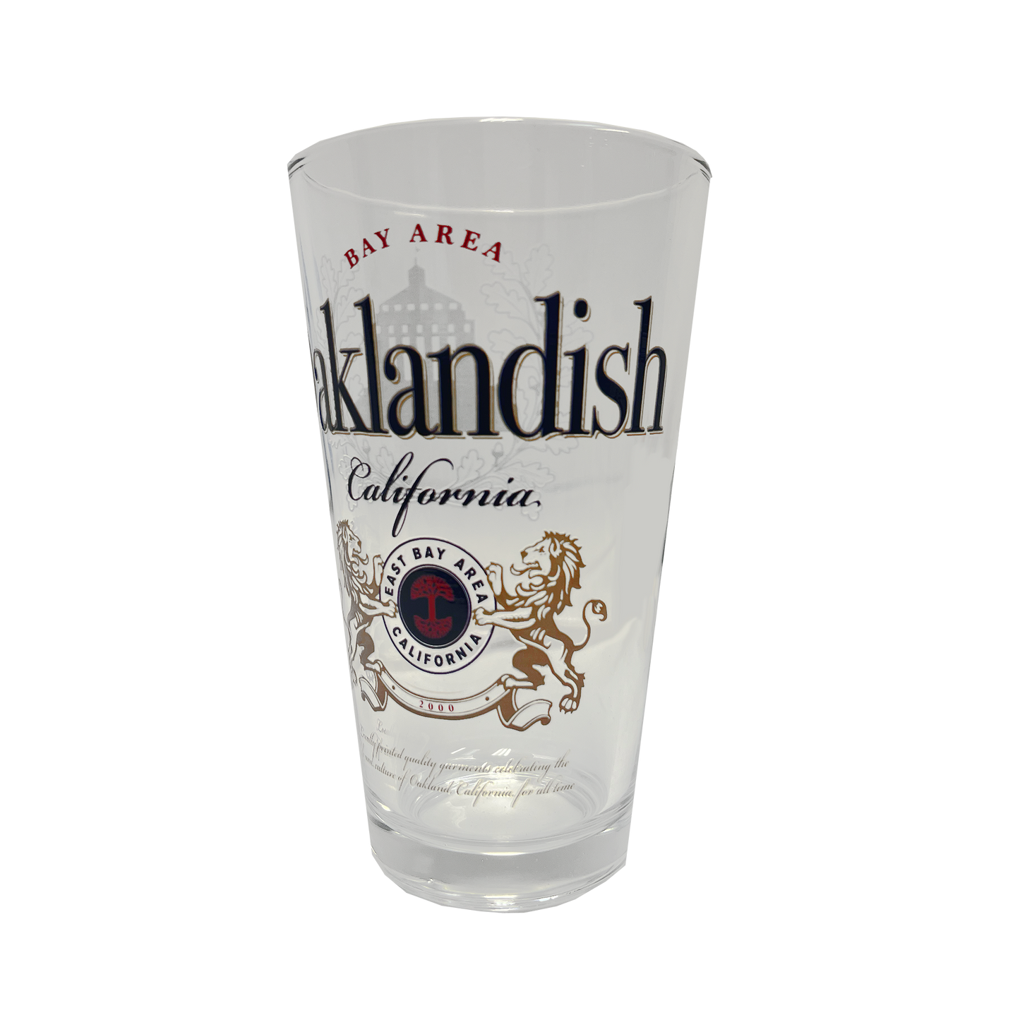 The **Lager Pint Glass** by **Oaklandish** is a stylish 16 oz pint glass featuring "Oaklandish" and "California" in bold black text. Above "Oaklandish," "Bay Area" is written in red, while below, a circular emblem displays "Bay Area California" flanked by two lions. The background of this practical drinkware is white, combining local pride with everyday functionality.