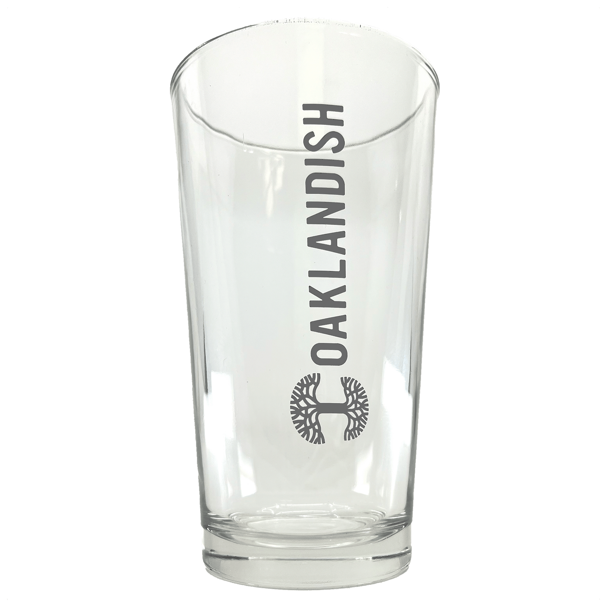 The Banner Pint Glass from Oaklandish is a clear drinking vessel with the word "OAKLANDISH" vertically inscribed in bold, black letters. Underneath this text, you'll find the brand's dark grey logo, a detailed circular tree design. The drinkware has a smooth, slightly tapered shape and features a thick base.