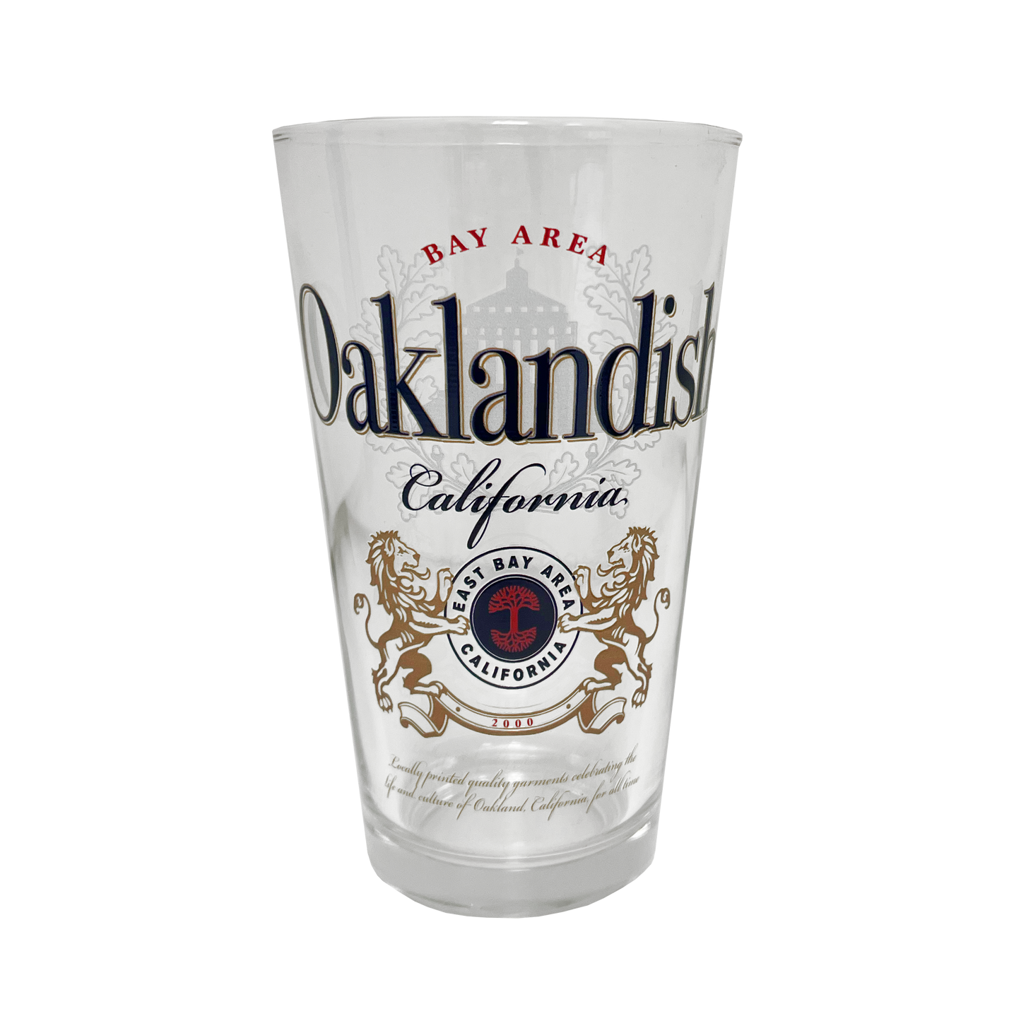 The Oaklandish Lager Pint Glass boasts a bold, ornate design with "Bay Area Oaklandish California" text. This 16 oz pint glass features a crest adorned with two golden lions facing each other, encircling a tree with the text “East Bay Area California.” Intricate design elements flawlessly blend text and graphics.