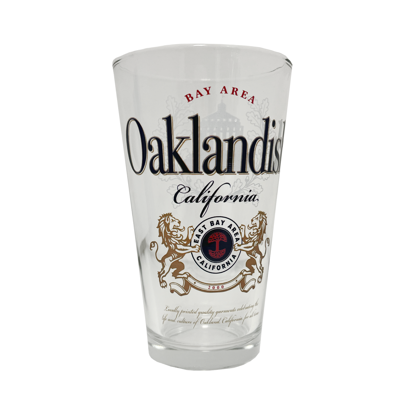 The Lager Pint Glass by Oaklandish is a 16 oz pint glass featuring the text "Bay Area Oaklandish California" in black and red. Below this, intricate graphics depict two lions standing on their hind legs, flanking a red and black emblem that reads "East Bay" and "California." Additional small text appears beneath the emblem, making it perfect for any drinkware collection.